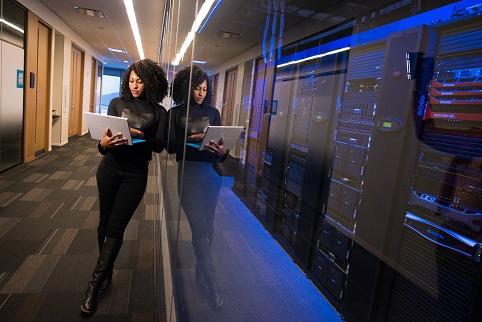 Woman next to servers holding and looking at laptop